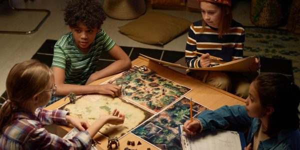 Les stratégies innovantes pour un jeu gratuit de strategie réussi Angle élevé de quatre amis interculturels jeunes discutant des règles et des stratégies du nouveau jeu de société tout en étant assis près de la table avec le conseil d'administration