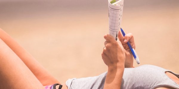 Vacances à la plage : quels jeux de casse-têtes emporter ? Belle femme se rapproche sur le corps et a bon moment à faire des mots jouer sur du papier.
